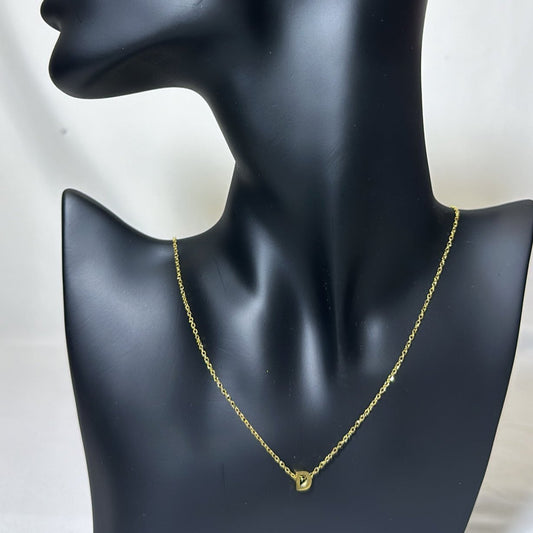 A matte black mannequin with a gold chain like piece and an alphabetic pendant on its burst on a light grey surface