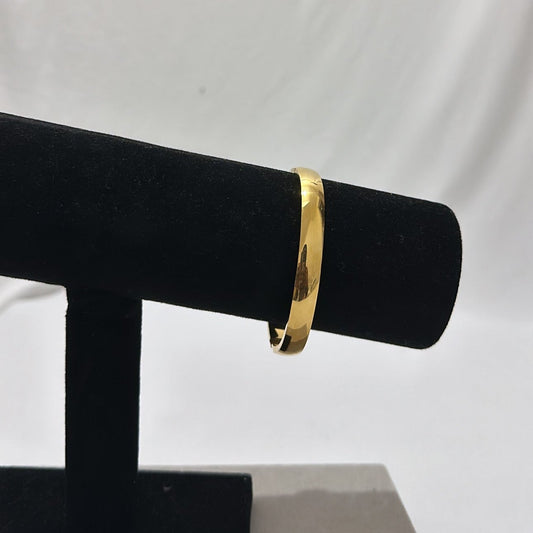 Elegant gold bangle bracelet displayed on a black velvet stand against a white background, showcasing luxury jewelry for fashion and style.