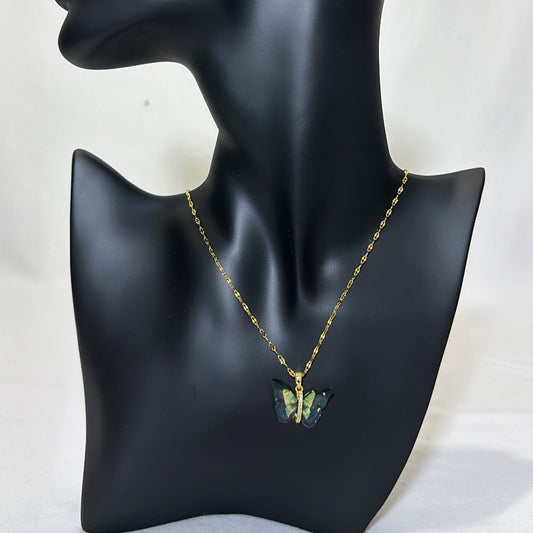 a black matte mannequin with a gold necklace piece around its neck with green gold like pendant, display on a light background.