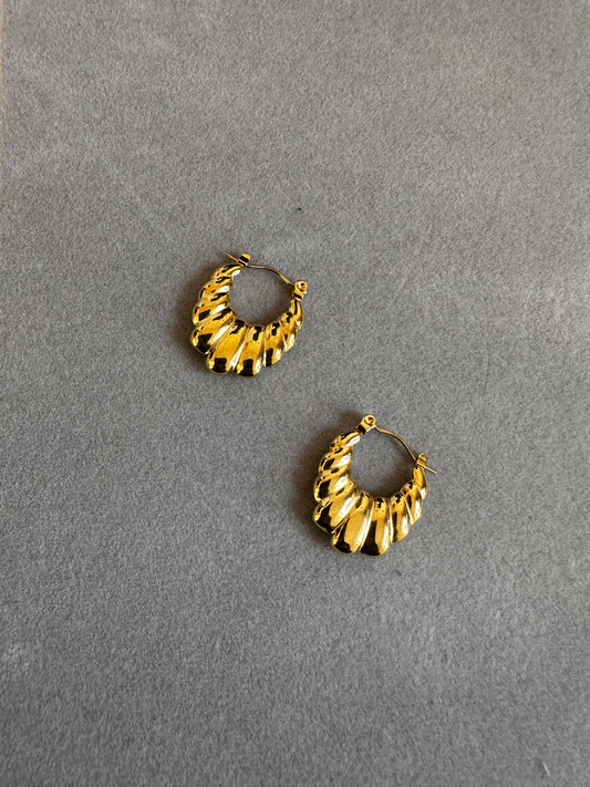 a pair of gold hop earring displayed featuring a ridge , fan like design. it had a plain and light background.