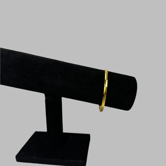 Elegant gold detailed bangle displayed on a black velvet jewelry stand against a white background, perfect for showcasing minimalist jewelry designs.