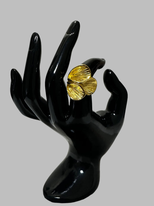 a hand shaped mannequin presents a gold leafy ring. Jewelry contrast against the black displays, with a soft light gray background